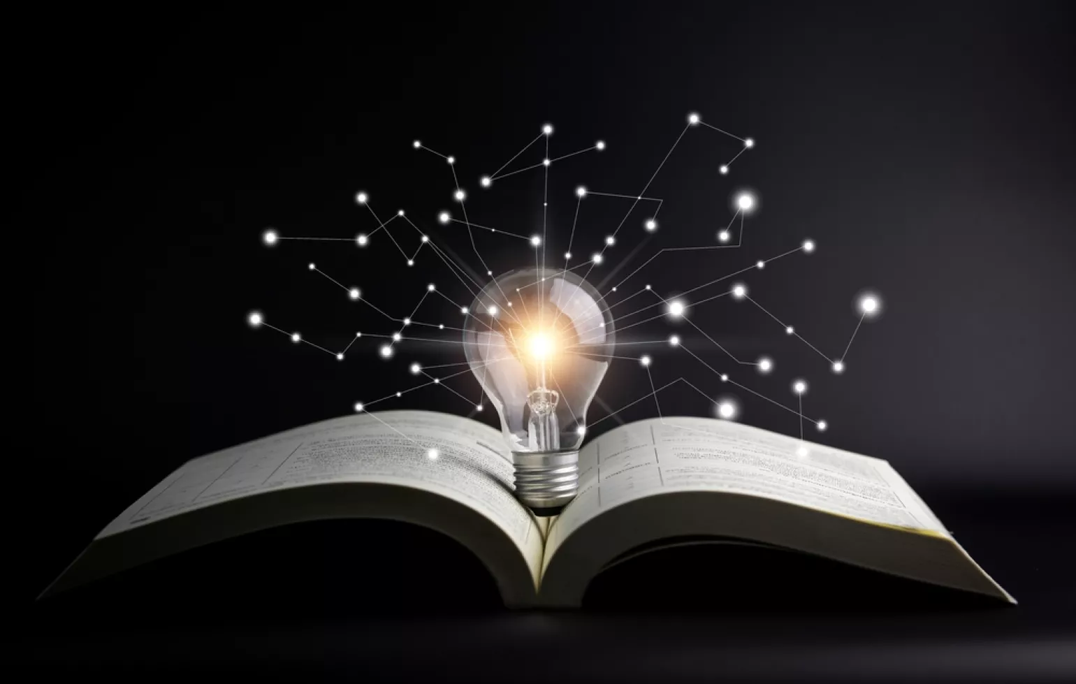 Open book against a black background with a light bulb emerging from the middle connecting to white dots