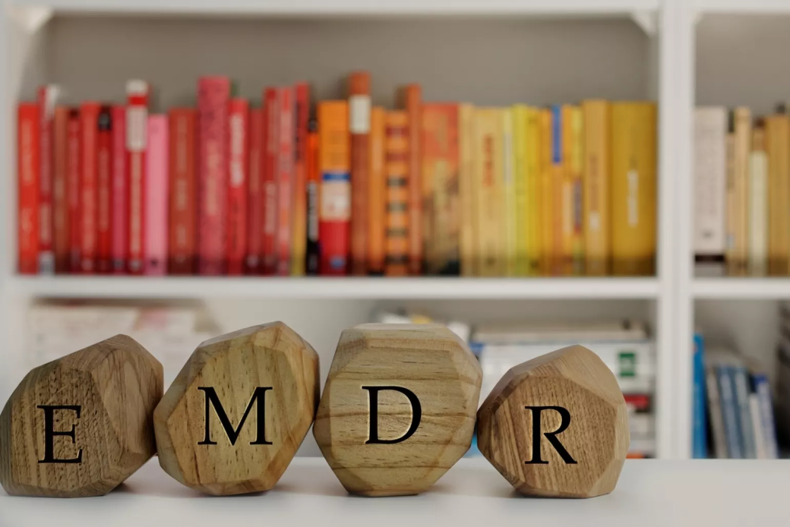 Wooden block letters that spell EMDR in an office with red and yellow books