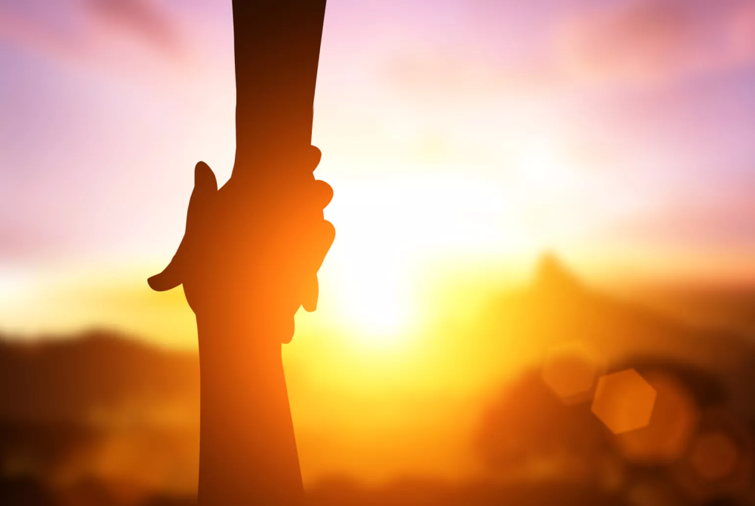 Silhouette of hands holding in front of a bright sunset