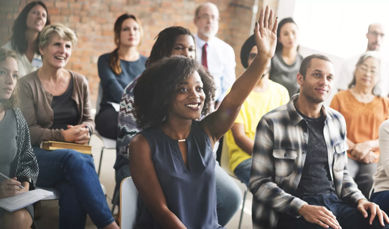 Diverse group of people in a room paying attention to a presentation, African American woman raising hand