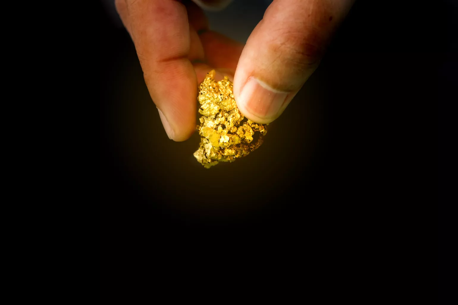 Two fingers holding a piece of gold, black background