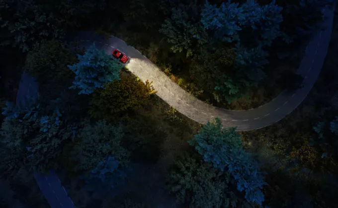 Aerial view of a red car headlights on deep forest road