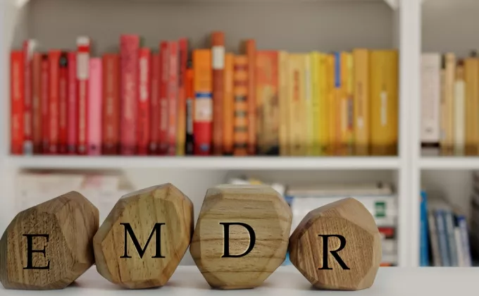 Wooden block letters that spell EMDR in an office with red and yellow books