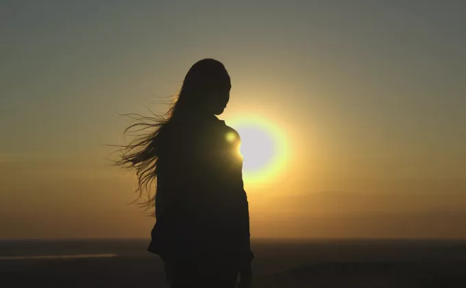 Young girl looks at sunset silhouette, hair blowing in the wind