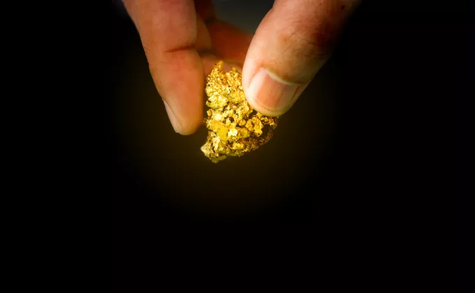 Two fingers holding a piece of gold, black background